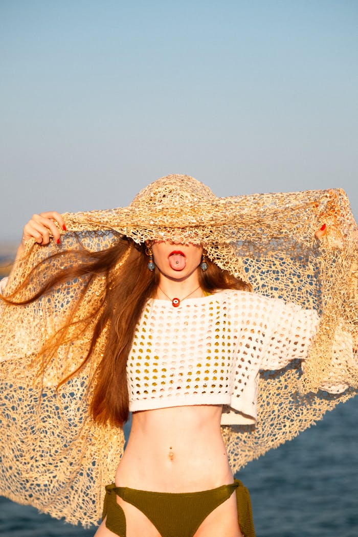 about-us A playful young woman in crochet fashion poses humorously by the seaside, embodying summer vibes.